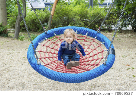 Cute little child having fun on a colorful swing outdoor in the park. Beautiful spring day in children playground Cute little child having fun on a colorful swing outdoor in the park. Beautiful spring day in children playground 78969527