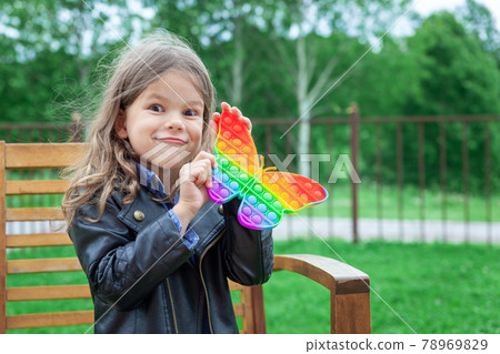 Caucasian little girl playing with pop it silicone trendy rainbow colow toy 78969829