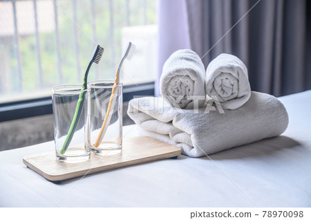 Set of hotel amenities (such as towels, drinking glass, toothbrush etc) on the bed. Hotel amenities is something of a premium nature provided in addition to the room when renting a room. Set of hotel amenities (such as towels, drinking glass, toothbrush etc) on the bed. Hotel amenities is something of a premium nature provided in addition to the room when renting a room. 78970098
