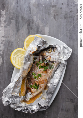 baked fish with lemon in aluminium foil on ceramic background baked fish with lemon in aluminium foil on ceramic background 78972004