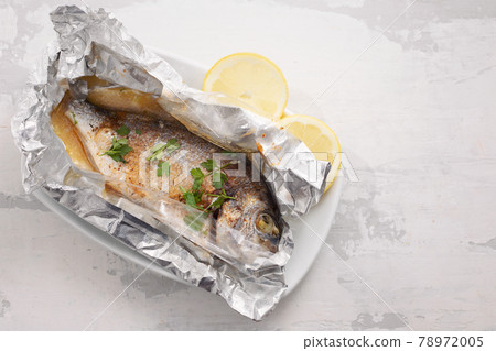 baked fish with lemon in aluminium foil on ceramic background baked fish with lemon in aluminium foil on ceramic background 78972005
