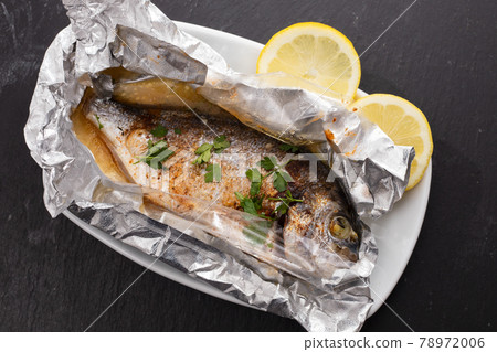 baked fish with lemon in aluminium foil on ceramic background 78972006