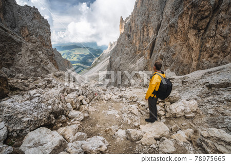 Man in yellow jacket and backpack at Pass on Mountain Sassolungo - Langkofel, Alpe di Siusi, Dolomiti mountain - South Tyrol, Italy, Europe, UNESCO World Heritage Site 78975665