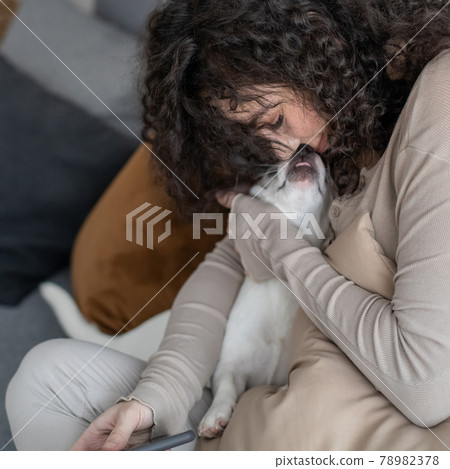 Cheerful curly woman kissing hugging little dog feeling love tenderness at cozy minimalistic home Cheerful curly woman kissing hugging little dog feeling love tenderness at cozy minimalistic home 78982378