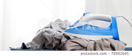 Electric iron and shirt on ironing board in laundry shop 78982695