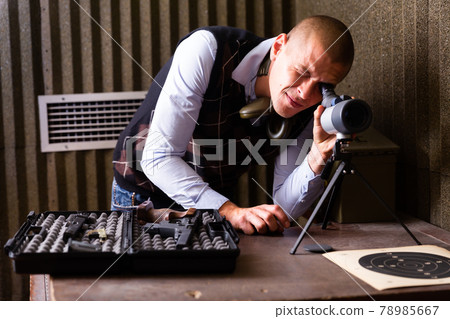 Instructor of shooting range looks through spyglass at target Instructor of shooting range looks through spyglass at target 78985667