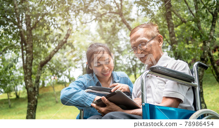 Grandfather in wheelchair and granddaughter having fun with digital tablet in the park. Family life on vacation. 78986454