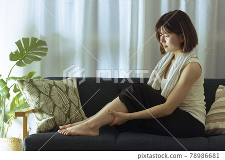 Young woman massaging calf in the living room Young woman massaging calf in the living room 78986681