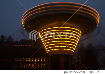 A blurry chain carousel in motion at the amusement park, night illumination. The effect of bokeh and long exposure. A blurry chain carousel in motion at the amusement park, night illumination. The effect of bokeh and long exposure. 78989243