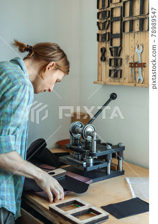 Male tanner working with handpress device machine cutting pattern on stuff material leather workshop Male tanner working with handpress device machine cutting pattern on stuff material leather workshop 78989547