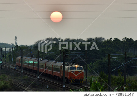 當太陽在天空中升起時，一列火車沿著村莊的鐵軌行駛。 78991147