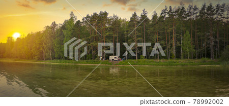 camper stands near the forest and lake. 78992002