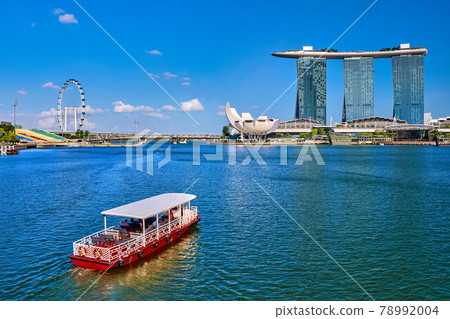 Tourist cruise boat navigating in Marina Bay, Singapore. iconic Marina Bay Sands, Shoppes mall, ArtScience museum, Helix bridge and Singapore Flyer.  78992004