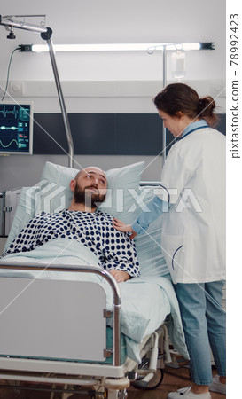 Sick man resting in bed while therapist doctor monitoring respiratory recovery Sick man resting in bed while therapist doctor monitoring respiratory recovery 78992423
