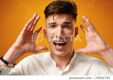 Stressed shouting young man holding hands near his head 78992745