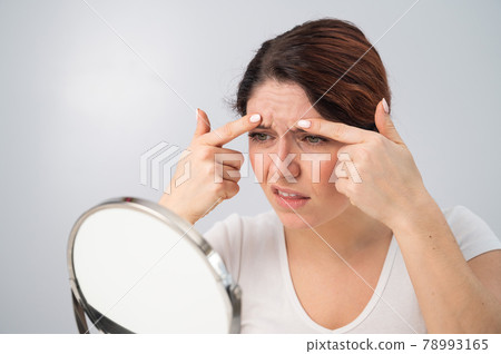 Caucasian woman looks at herself in the mirror and is upset because of facial wrinkles on her face. 78993165