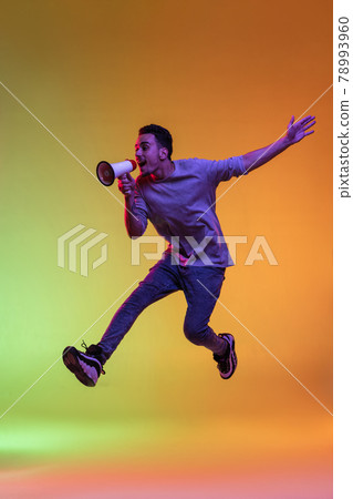 One Latina young man with megaphone, loudspeaker jumping high isolated on gradient yellow green background in neon light. One Latina young man with megaphone, loudspeaker jumping high isolated on gradient yellow green background in neon light. 78993960