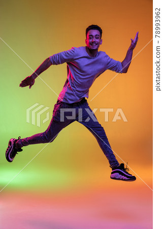 Full length portrait of Latina young man jumping high isolated on gradient yellow green background in neon light. 78993962
