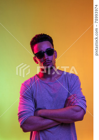 Portrait of Latina young man in sun glasses posing isolated on gradient yellow green background in neon light. 78993974