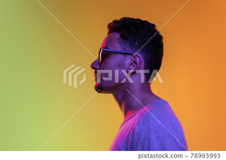 Portrait of Latina young man in sun glasses posing isolated on gradient yellow green background in neon light. Side view 78993993