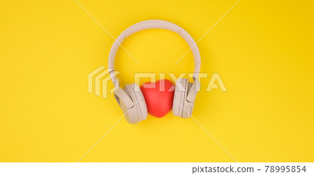 red heart and beige wireless headphones on a yellow background 78995854