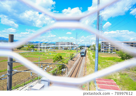 A train that stops at an unmanned station in the countryside, viewed from the gap in the fence of the pedestrian bridge 78997612