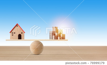 Model house on seesaw balancing with stacking coins money on blue background. Property investment and home mortgage financial real estate advertising concept Model house on seesaw balancing with stacking coins money on blue background. Property investment and home mortgage financial real estate advertising concept 78999179