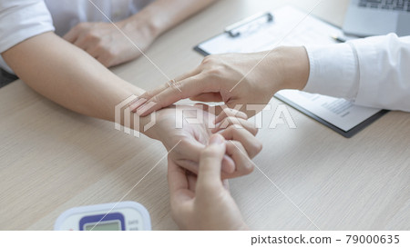 Medical professional measures the pulse of a male patient's wrist to check his heart rate in the hospital's examination room, Doctor checking patient health, Initial symptom check. Medical professional measures the pulse of a male patient's wrist to check his heart rate in the hospital's examination room, Doctor checking patient health, Initial symptom check. 79000635