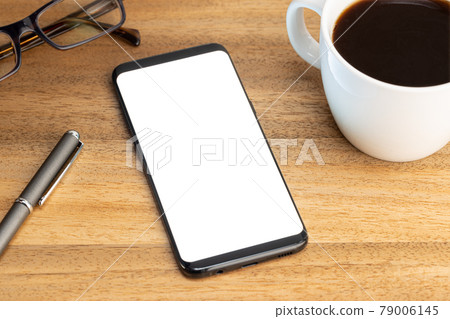 Smartphone mockup template with coffee cup and eyeglasses on wooden table. White screen Smartphone mockup template with coffee cup and eyeglasses on wooden table. White screen 79006145