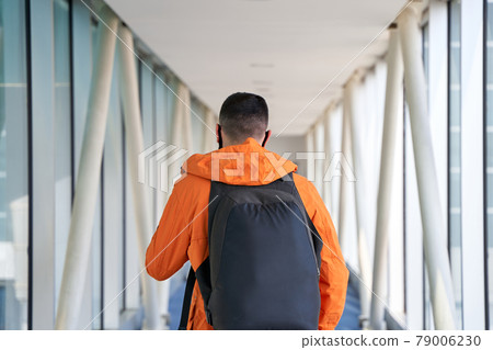 Guy tourist with a backpack and in a medical mask is walking along the airbridge from the plane to the airport terminal Guy tourist with a backpack and in a medical mask is walking along the airbridge from the plane to the airport terminal 79006230