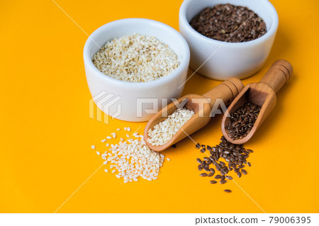 Wooden spoons with flax and sesame seeds lies in a white mortar on a yellow background. Healthy eating. Keto diet. 79006395