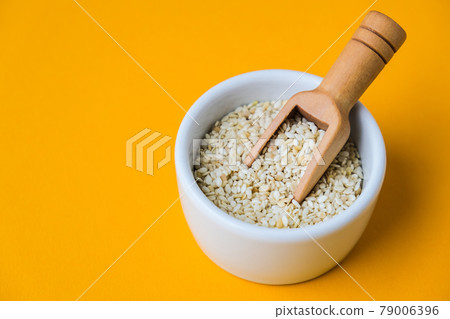 Wooden spoon with sesame seeds lies in a white mortar on a yellow background. Healthy eating. Keto diet. 79006396