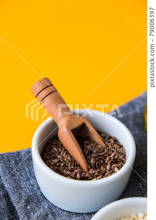 Wooden spoon with flax seeds lies in a white mortar on a yellow background. Healthy eating. Keto diet. 79006397