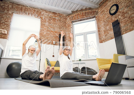 Mature couple sitting in staff yoga pose and using laptop Mature couple sitting in staff yoga pose and using laptop 79006568