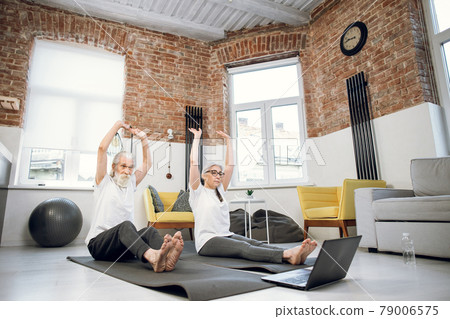 Aged couple using laptop for practising dandasana pose Aged couple using laptop for practising dandasana pose 79006575