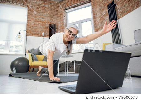 Retired woman using laptop and doing yoga at home Retired woman using laptop and doing yoga at home 79006578
