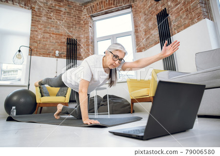 Retired woman using laptop and doing yoga at home Retired woman using laptop and doing yoga at home 79006580