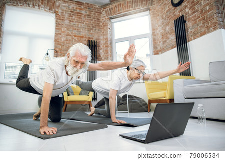 Elderly couple using laptop for doing yogat at home Elderly couple using laptop for doing yogat at home 79006584