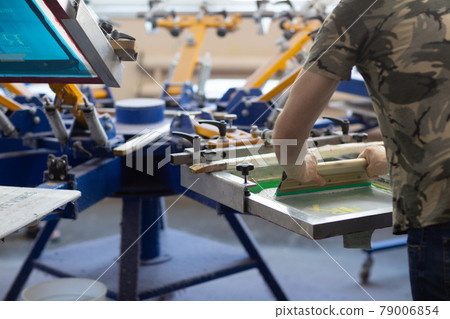 Serigraphy silk screen print process at clothes factory. Frame, squeegee and plastisol color paints Serigraphy silk screen print process at clothes factory. Frame, squeegee and plastisol color paints 79006854