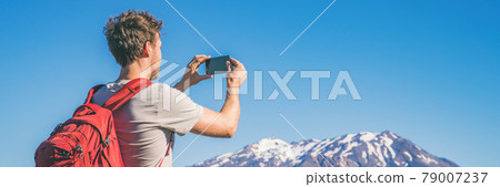 Travel tourist hiking man taking picture with phone of mountains landscape on summer hike adventure. Panorama banner with copy space on blue sky background 79007237
