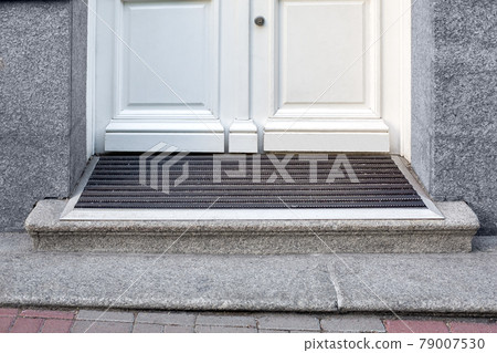 stone threshold with foot mat at the entrance door made of white wood and gray stone facade cladding of retro European architecture building close-up front view, nobody. 79007530