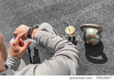 Gym fitness strength training fit man using sport watch smartwatch touchscreen at kettlebell weight lifting workout. green smoothie athlete healthy fitness lifestyle 79010807