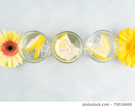 Lemon water drink with ice cubes on stone background with gerbera daisy yellow flowers 79016669