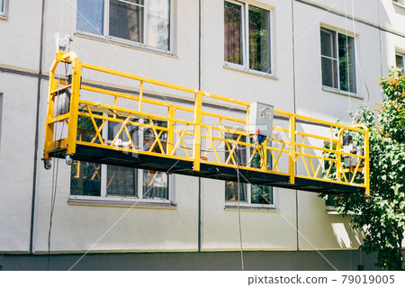 Suspended construction cradle. Facing, repair, maintenance, painting the building in sunny summertime. Suspended construction cradle. Facing, repair, maintenance, painting the building in sunny summertime. 79019005