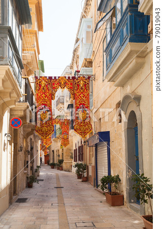 Old narrow street, perspective view with colorful flags decoration, Valletta 79019043