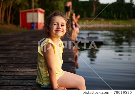 Happy girl on a pier smiles looking at camera. Summer leisure activities concepts. Heat summer, summer evenings in nature, spending time in the fresh air 79019550