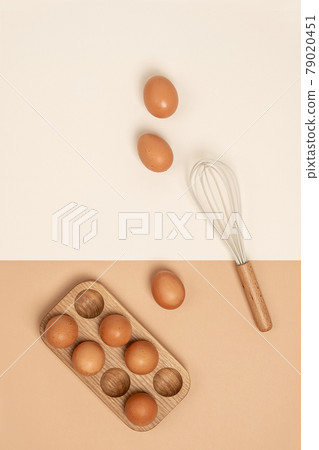Eggs in wooden egg box and whisk on beige background. Flat lay Top view Copy space 79020451