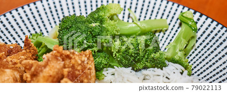 Close-up of cooked green broccoli at the edge of a plate with rice and fried meat 79022113