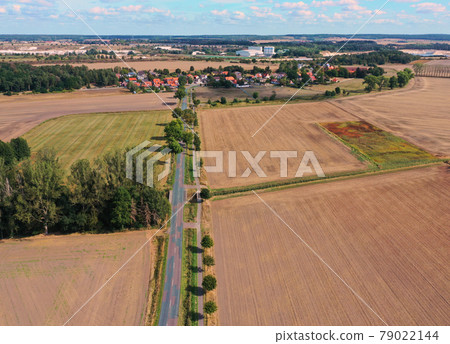 Aerial view of a straight country road leading to a village in a cultural landscape of monotonous arable land. Aerial view of a straight country road leading to a village in a cultural landscape of monotonous arable land. 79022144