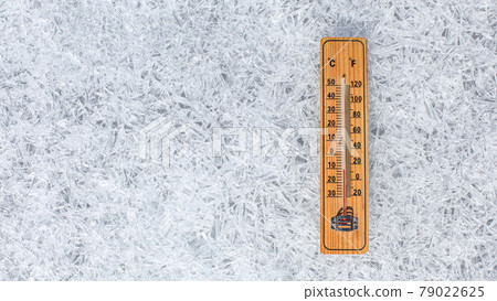 Wooden thermometer showing low temperature laying on flat ice ground made of crystals. Winter weather concept. 79022625